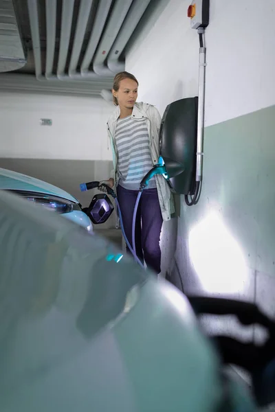 Mujer joven cargando un vehículo eléctrico en un garaje subterráneo — Foto de Stock