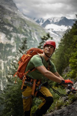 Ferrata rotasındaki genç, erkek tırmanıcı İsviçre Alplerinde bir kayaya tırmanıyor.