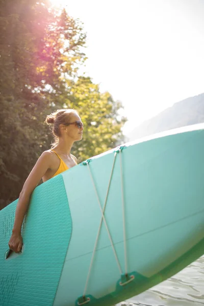 湖の上のパドルボードに乗って美しい夏の日を楽しんでいる若い女性 — ストック写真