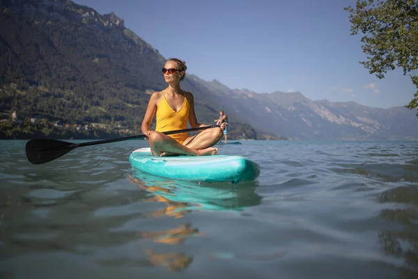 Supスタンドアップパドルボードのコンセプト 暖かい午後の光の中で美しい湖に乗ってかわいい 若い女性のパドルボード 水中から撮影 — ストック写真
