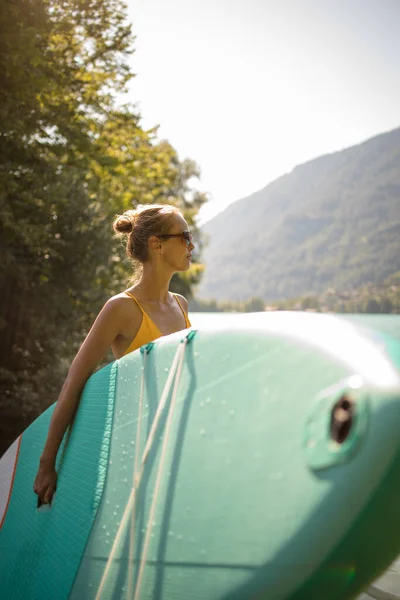 湖の上のパドルボードに乗って美しい夏の日を楽しんでいる若い女性 — ストック写真