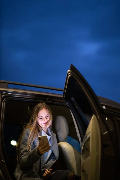 年轻女人拿着手机坐在车后座上准备旅行 彩色调的图像 浅色的Dof — 图库照片