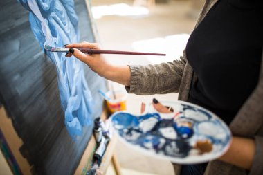 Palet ve boya fırçası sanatçının ellerinde. Ressam, el paletinde boya fırçasıyla yağlı boya resim çiziyor. Palet ve boya fırçasını elinde tutan sanatçı. Sanatçılar paletle boya fırçası.