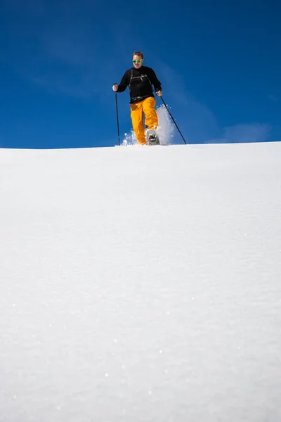 冬季运动 年轻男子穿着雪鞋跑下山 高山上覆盖着大雪 — 图库照片