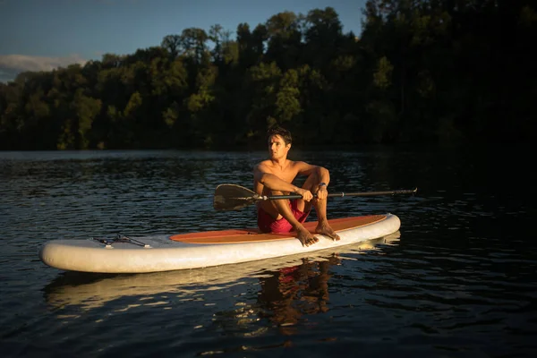 パドルボードの若い男 暖かい夜の日差しの中で美しい川で素晴らしい運動を得る パドル水中画像 — ストック写真