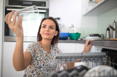 Güzel, genç bir kadın bulaşık makinesine bulaşık koyuyor (sığ DOF; renk tonlu resim)