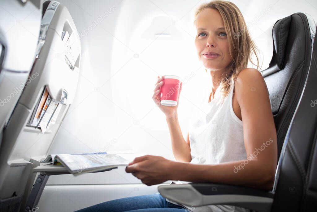 Young happy woman taking selfie photo with passport document sitting on the aircraft seat near a window during the flight in the airplane