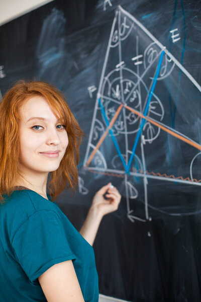 Portrait of a pretty young college student writing on the blackboard during a maths class (color toned image)