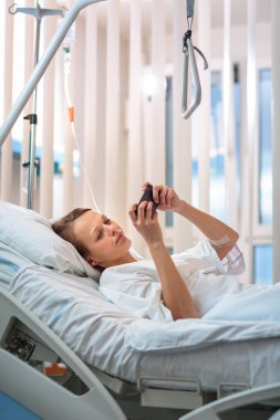 Modern bir hastane odasında güzel, genç, bayan bir hasta. Ameliyattan sonra hızla iyileşmek - düşünceli ama olumlu, ileriyi düşünen, planlar yapan (sığ DOF; renk tonlu görüntü))