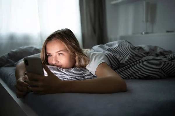 かなり若い女性が彼女の近くの彼女の携帯電話で彼女のベッドで寝ていた ベッドのスマートフォン スマートフォンの中毒コンセプト — ストック写真