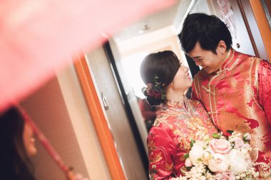 Mutlu Asyalı gelin ve damat düğün ulusal geleneksel kostümler içinde el ele tutuşup odada duruyor, düğün konsepti  