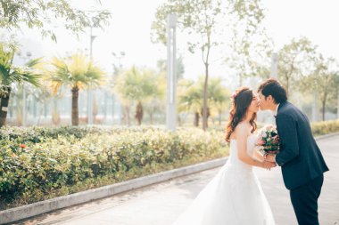 Mutlu gelin ve damat öpüşürken güneşli bir günde parkın yanında, düğün konsepti 