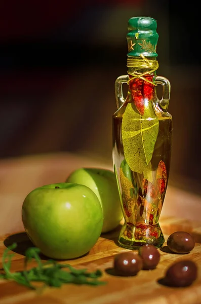 Olive oil bottle with spices in with green apples and olives in the background