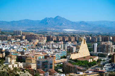 Panoramik şehir Santa Barbara Kalesi: Alicante, İspanya. Blok apartmanlar, dağ, parklar, yollar, evler, palmiyeler. Arka plan, mavi gökyüzü güzel dağ manzarası
