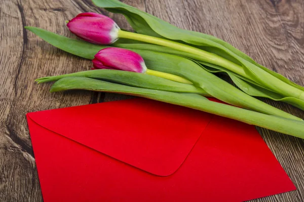 Rött kuvert med tulpaner på skrivbord trä — Stockfoto
