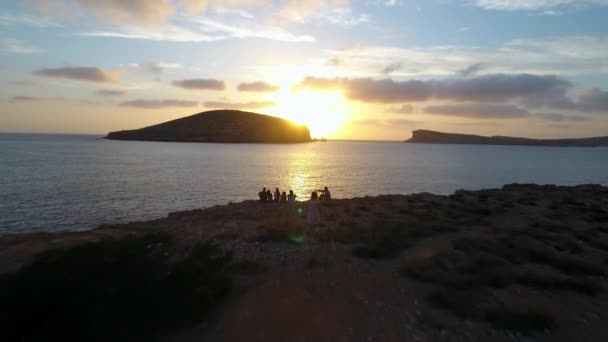 Друзів на скелях, спостерігаючи захід сонця над морем — стокове відео