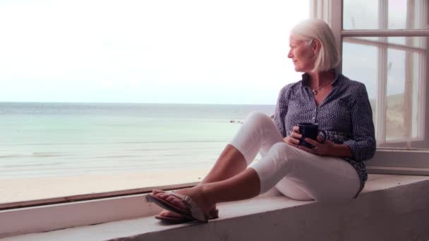 Γυναίκα κάθεται στο παράθυρο και κοιτάζοντας παραλία — Αρχείο Βίντεο