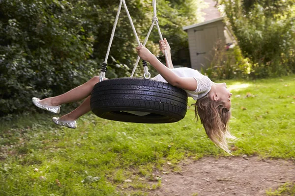 Giovane ragazza giocare su pneumatico swing in giardino — Foto Stock