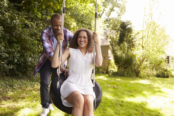 Uomo spingendo donna su pneumatico swing in giardino — Foto Stock