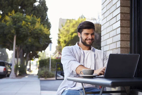 Bärtiger junger Mann mit Laptop an einem Tisch vor einem Café — Stockfoto