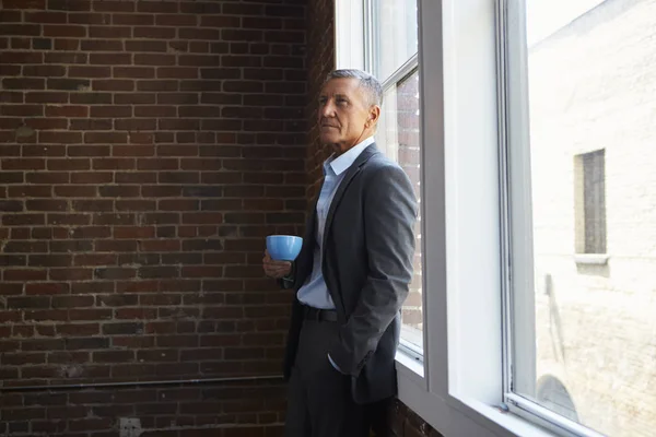 Ώριμες επιχειρηματία στέκεται από το παράθυρο του γραφείου με καφέ — Φωτογραφία Αρχείου