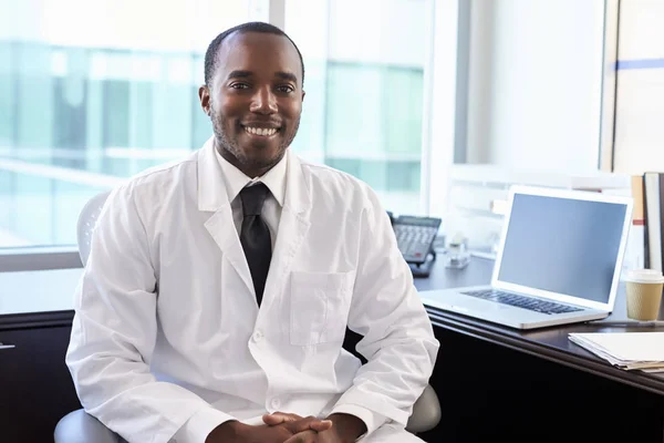 Arzt in weißem Mantel sitzt am Schreibtisch — Stockfoto