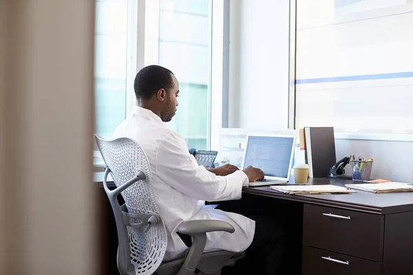 Doktor v bílém plášti sedí u stolu — Stock fotografie