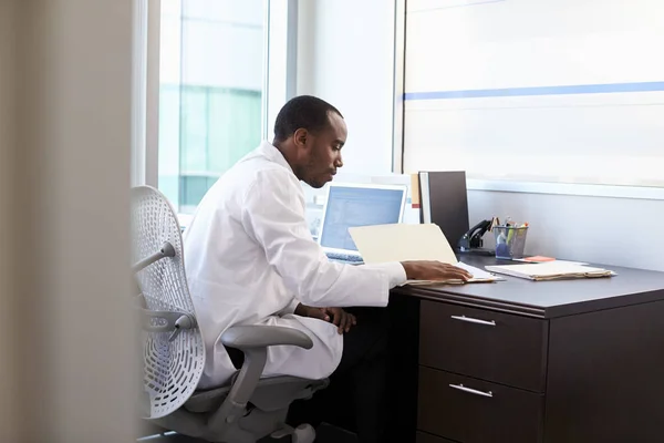 Arzt in weißem Mantel sitzt am Schreibtisch — Stockfoto