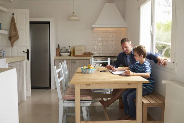 Hijo escribiendo en papel en la mesa de la cocina — Foto de Stock