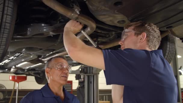 Mechanik a mužské stážista pracuje pod auto — Stock video