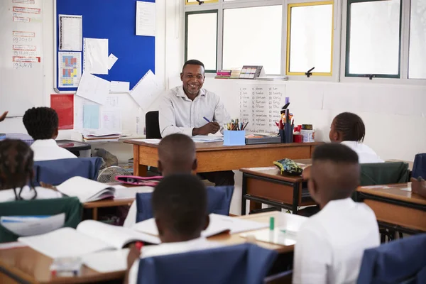 Profesor y niños sentados en escritorios — Foto de Stock