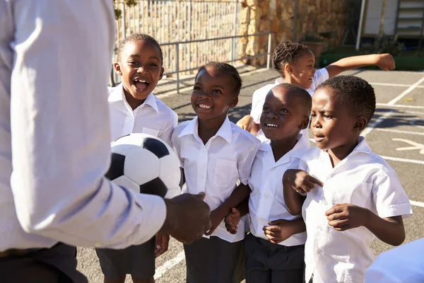 Учитель с мячом и детьми на школьной площадке — стоковое фото