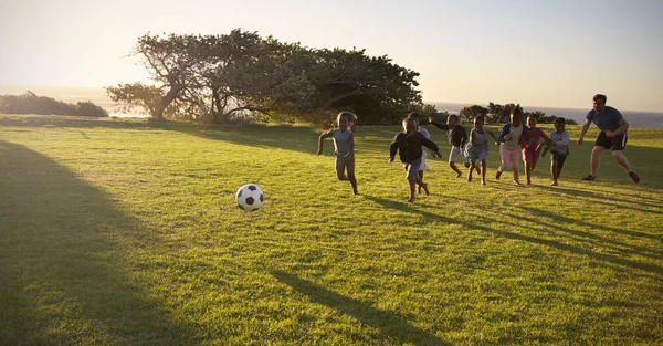 Opettaja ja koulun lapset pelaavat jalkapalloa — kuvapankkivalokuva