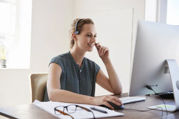 Усміхнена жінка за комп'ютером в офісі — стокове фото