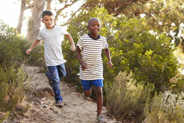 Due giovani ragazzi felici che corrono lungo un sentiero nel bosco — Foto Stock