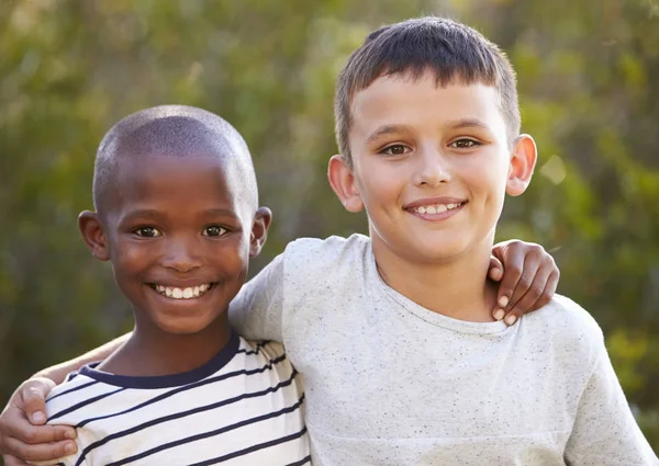 Два мальчика, обнимающие друг друга, улыбающиеся в камеру на улице — стоковое фото