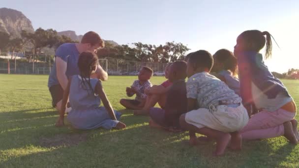 Kinder und Lehrer sitzen im Feld — Stockvideo