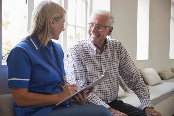 Hombre mayor se sienta con la enfermera haciendo notas en casa de retiro —  Fotos de Stock
