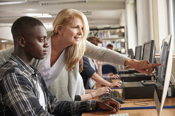 Lehrer mit männlichen Studenten, die in der Hochschulbibliothek am Computer arbeiten — Stockfoto