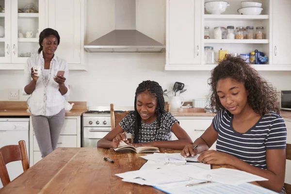 Madre usa el teléfono mientras las hijas se sientan a la mesa —  Fotos de Stock