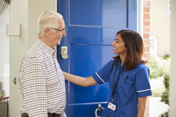Enfermeira em visita domiciliar cumprimentando o homem idoso — Fotografia de Stock