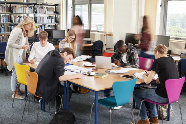 Učitel pomáhá studentů u stolu — Stock fotografie