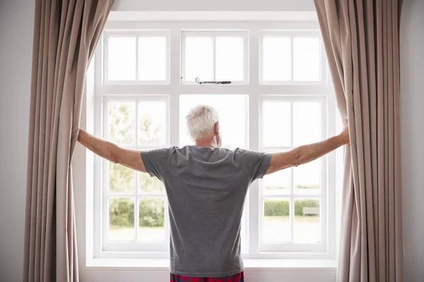 Senior Mann öffnet Schlafzimmervorhänge — Stockfoto