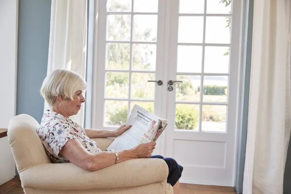 Senior Vrouw Zitten Stoel Het Lezen Van Een Krant Thuis — Stockfoto