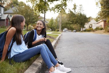 Two teen girlfriends sit talking at the roadside clipart