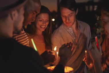 Friends on a rooftop lighting candles on a birthday cake clipart