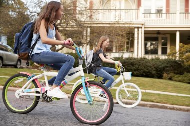 Two teen girls riding bikes in street, side view close up clipart