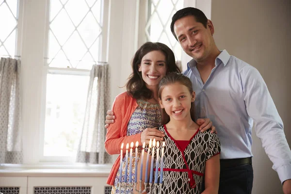 Jewish parents and daughter smiling, lit candles on menorah