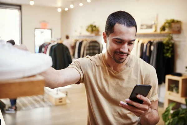 微笑的拉美裔男子使用智能手机在服装店 — 图库照片
