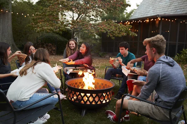 十几岁的朋友围坐在火坑边吃着带走的披萨 — 图库照片